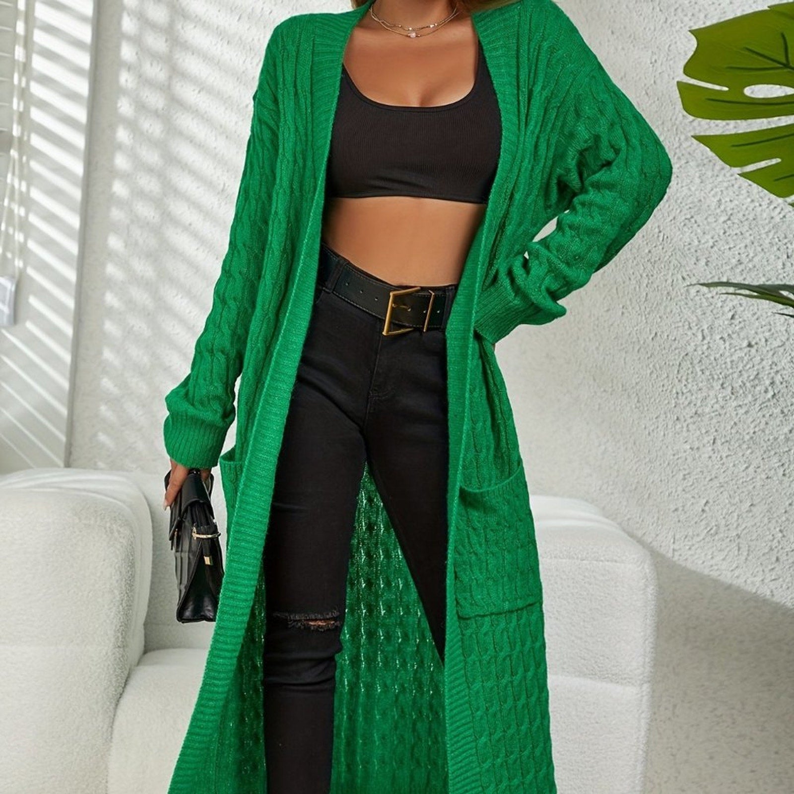 Person wearing a green cardigan over a black outfit with a white background