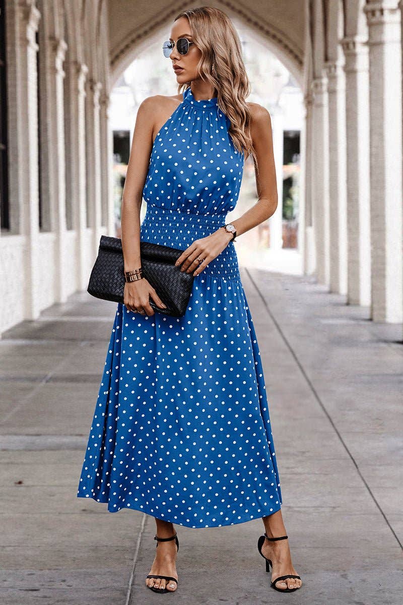 Woman wearing a blue polka dot dress with a black clutch in an outdoor setting.