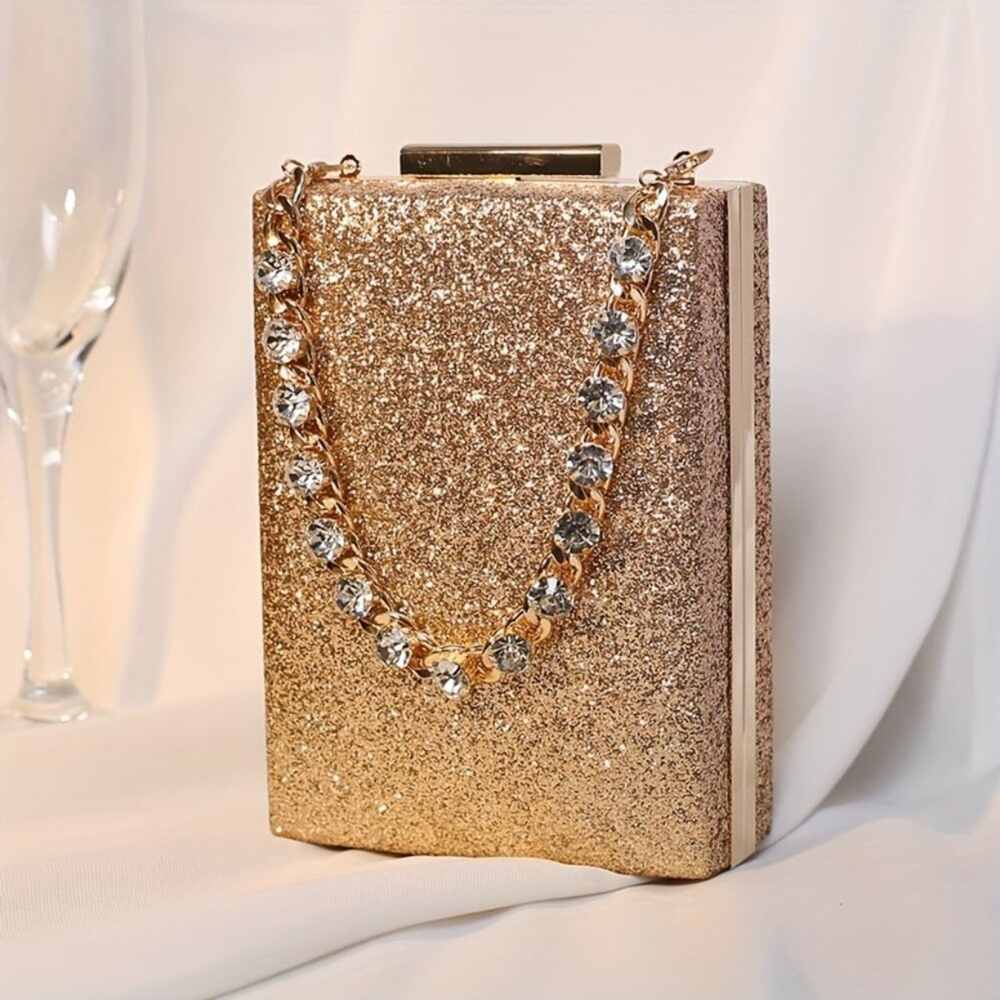 Gold glittery clutch bag with a chain strap on a white background