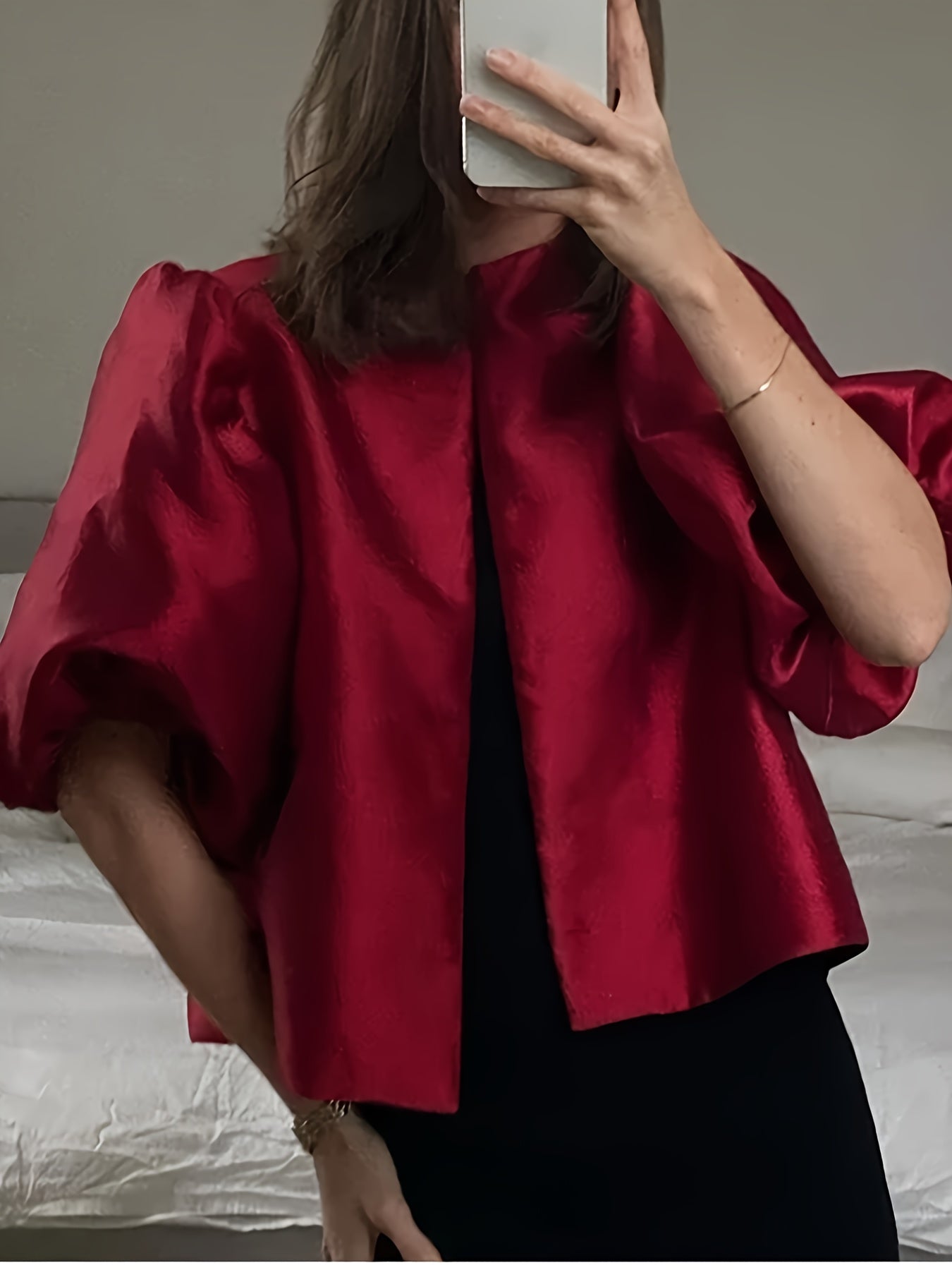 Person wearing a red satin top with puffed sleeves, holding a phone.