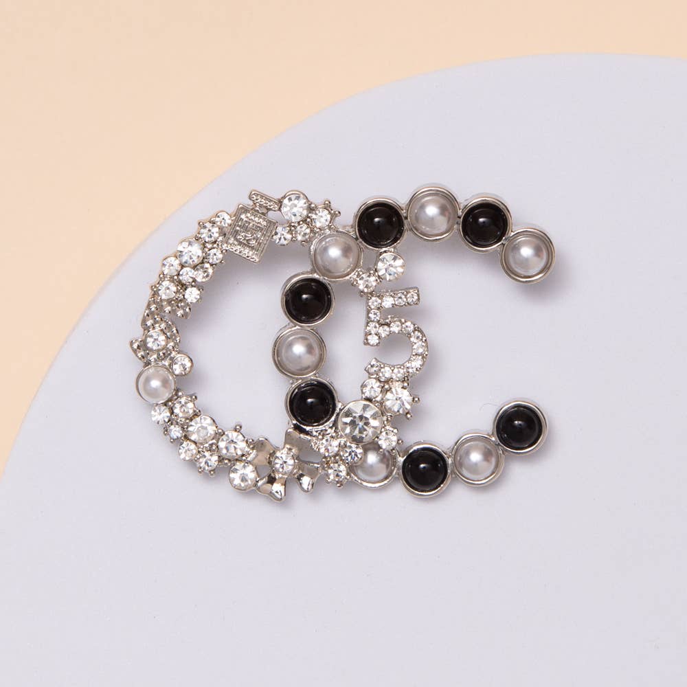 Set of three decorative brooches with pearls and black stones on a light blue background