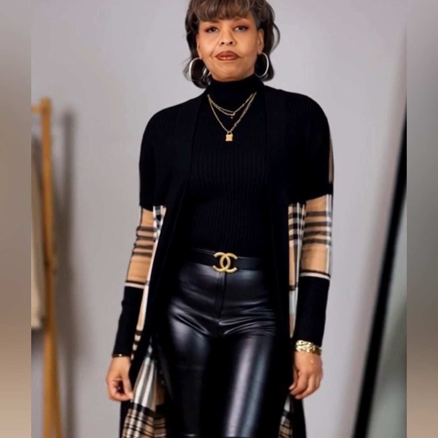 Person wearing a black ribbed sweater with sheer sleeves, black leather pants, and gold accessories.