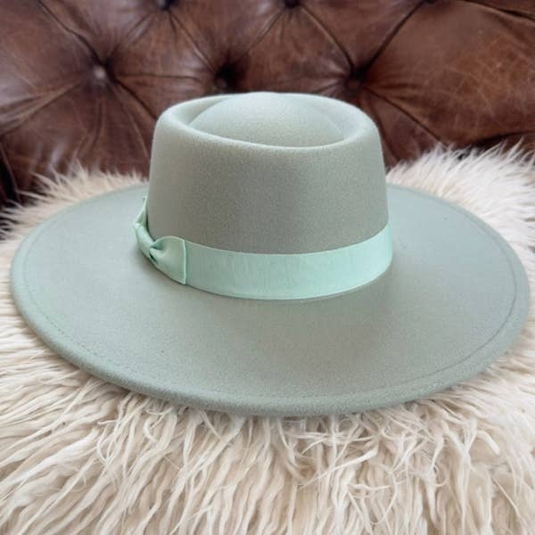 Light green fedora hat with a matching band on a fluffy beige surface with a brown leather couch in the background.