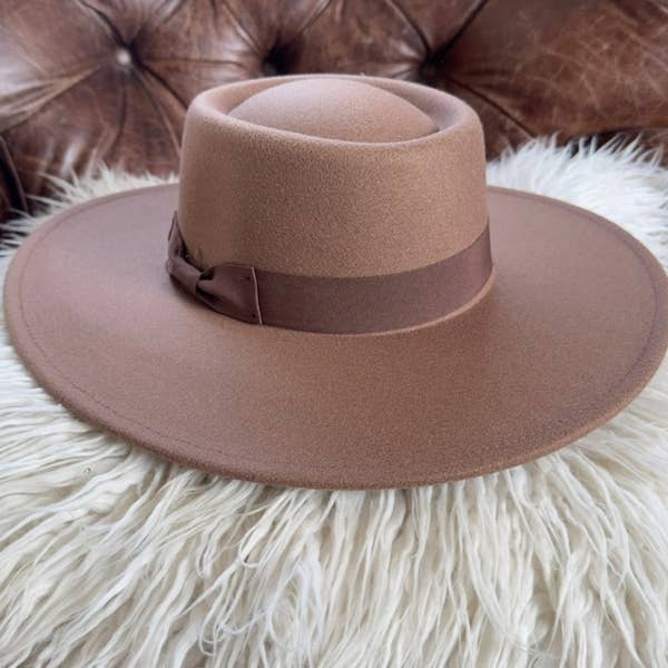 Brown fedora hat with a wide brim on a fluffy white surface.