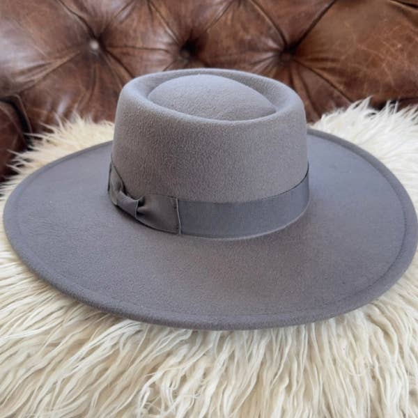 Gray fedora hat with a wide brim on a fluffy white surface with a brown leather background.