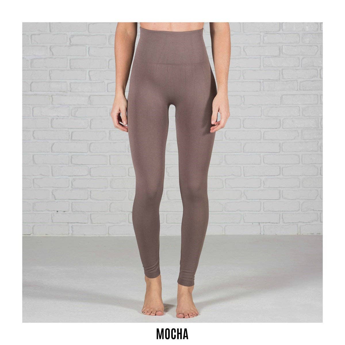 Mocha leggings worn by a person against a light gray brick wall.