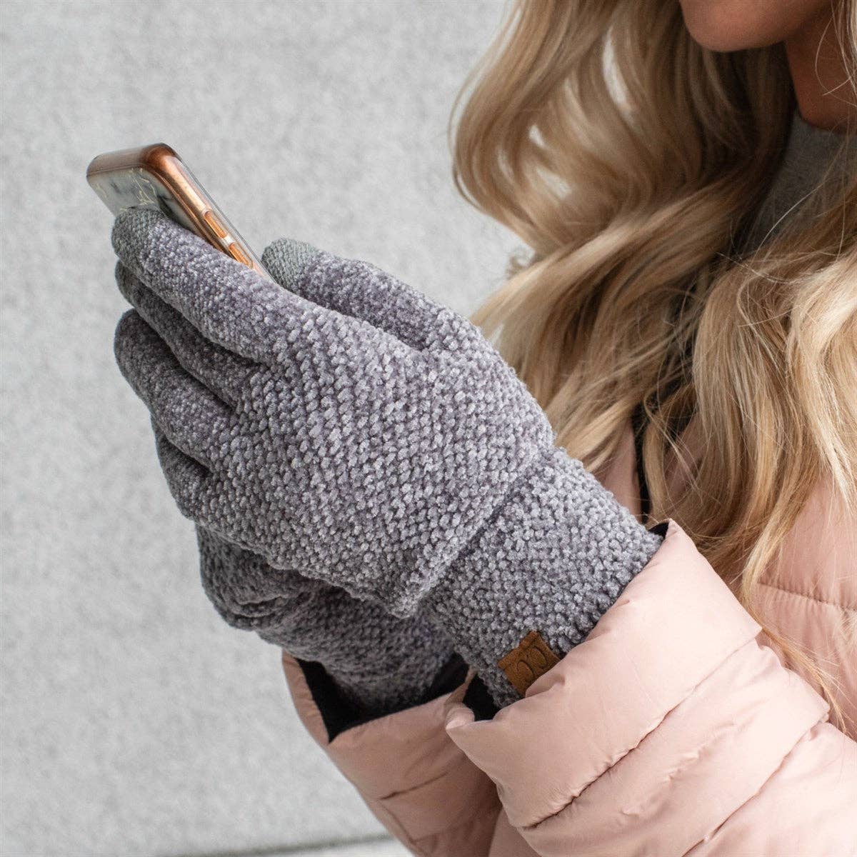 Person wearing gray textured gloves using a smartphone with a light gray background