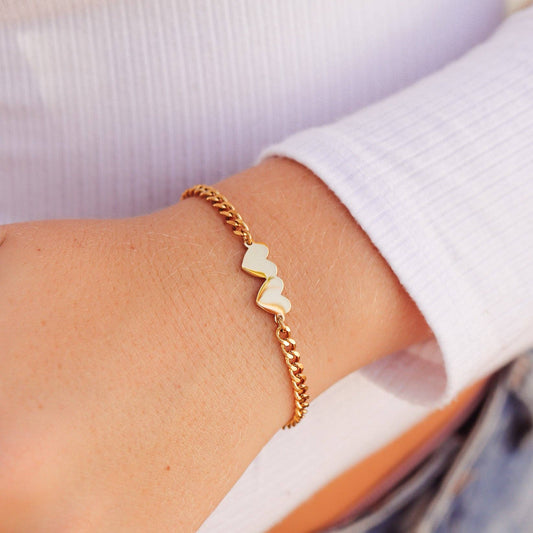 Gold bracelet with heart-shaped charms on a wrist against a white background