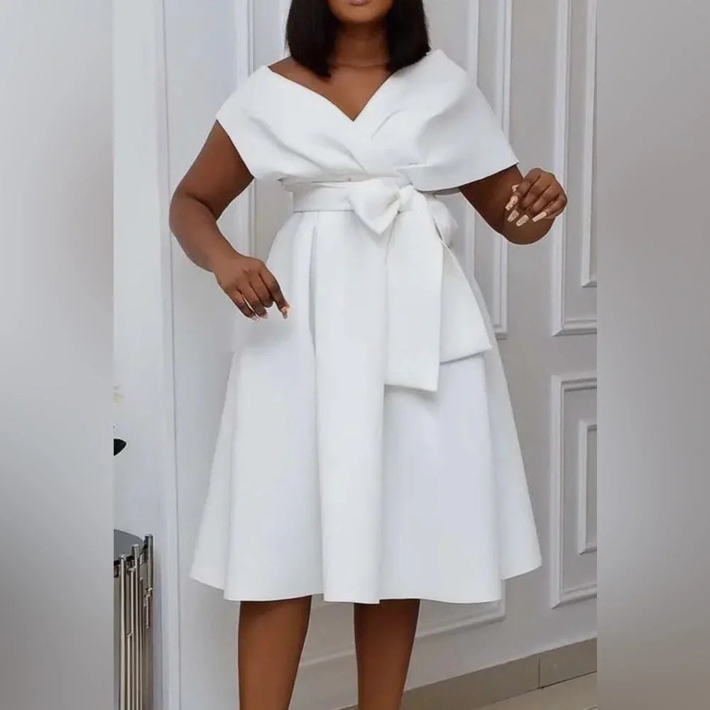 Woman wearing a white dress with a bow detail in a neutral setting