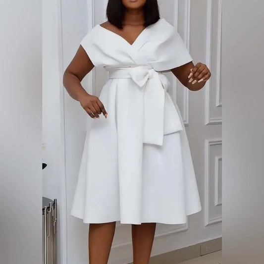 Woman wearing a white dress with a bow detail in a neutral setting