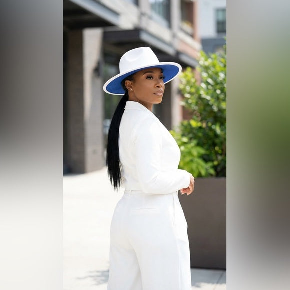 Woman in a white outfit and blue hat standing outdoors with blurred background