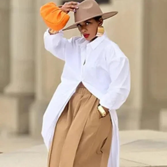 Person wearing a white shirt, beige hat, and tan pants with an orange object in a blurred architectural background