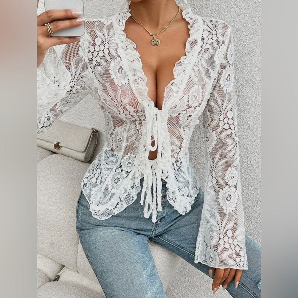 Person wearing a white lace top over a black garment, sitting on a couch.