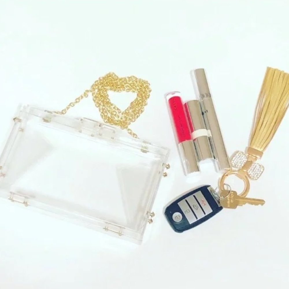 Clear pouch with gold chain, lipsticks, keychain, and tassel on a white background