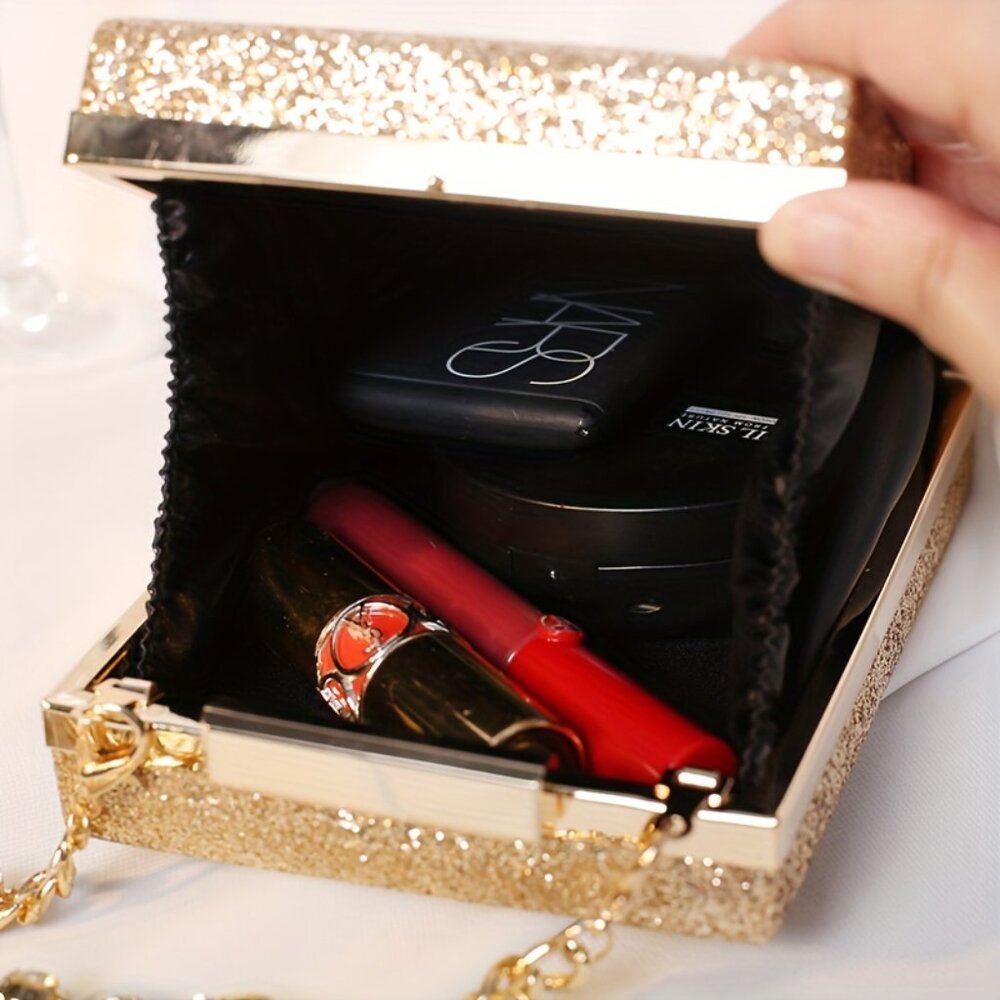 Gold glittery box with makeup items including a red lip gloss and black compact mirror.