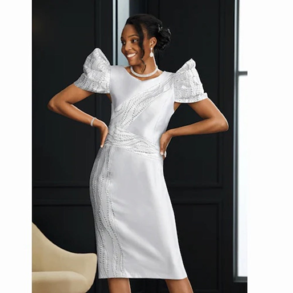 Woman wearing a white dress with lace details in a room with a black door and beige chair.
