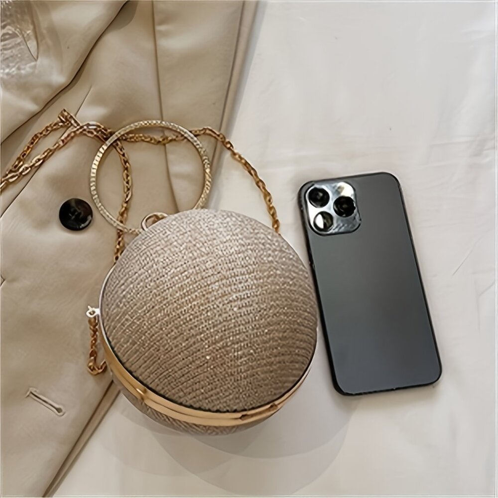 Round woven handbag with gold chain and black phone on a light background
