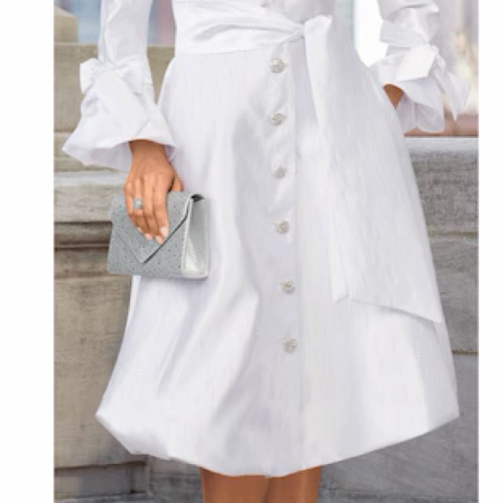 White dress with buttons and a gray clutch held by a person on stone steps.