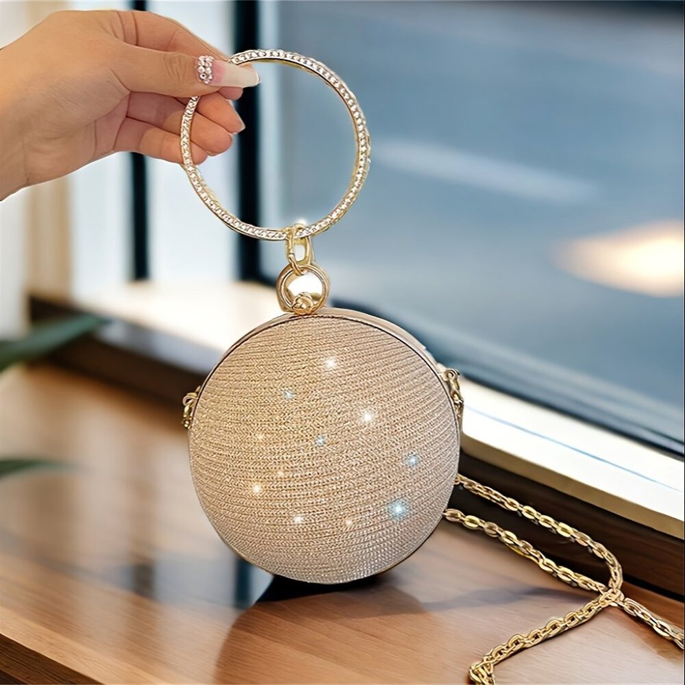 Gold round handbag with rhinestone details held by a hand on a blurred indoor background