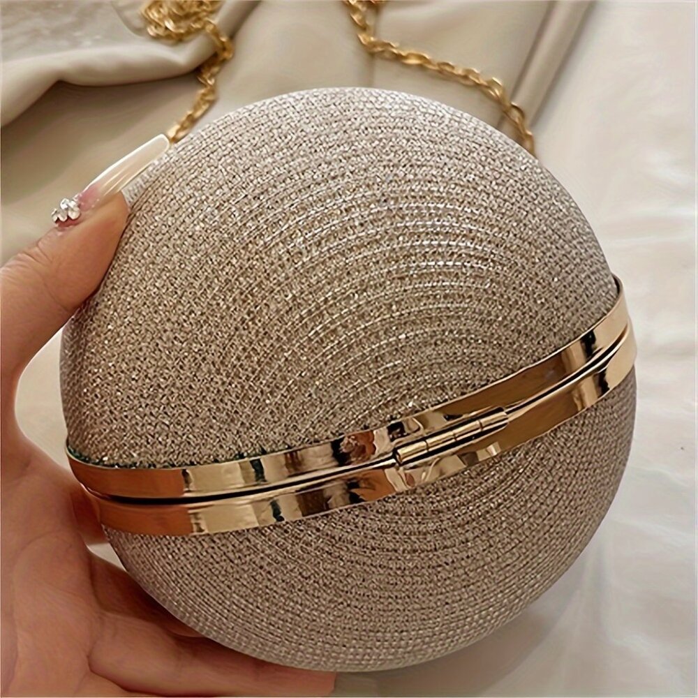 Gold glittery spherical handbag held by a hand against a neutral background