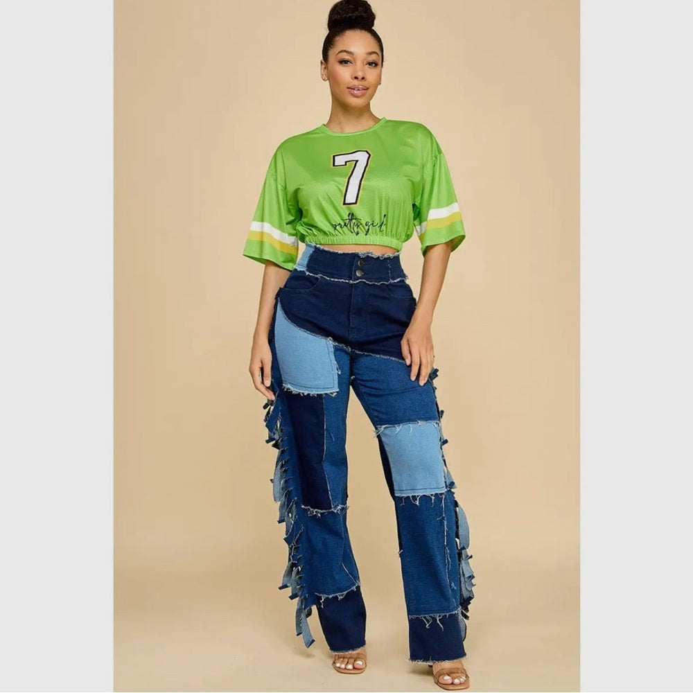 Woman wearing a green crop top with the number 7 and blue patchwork jeans on a beige background