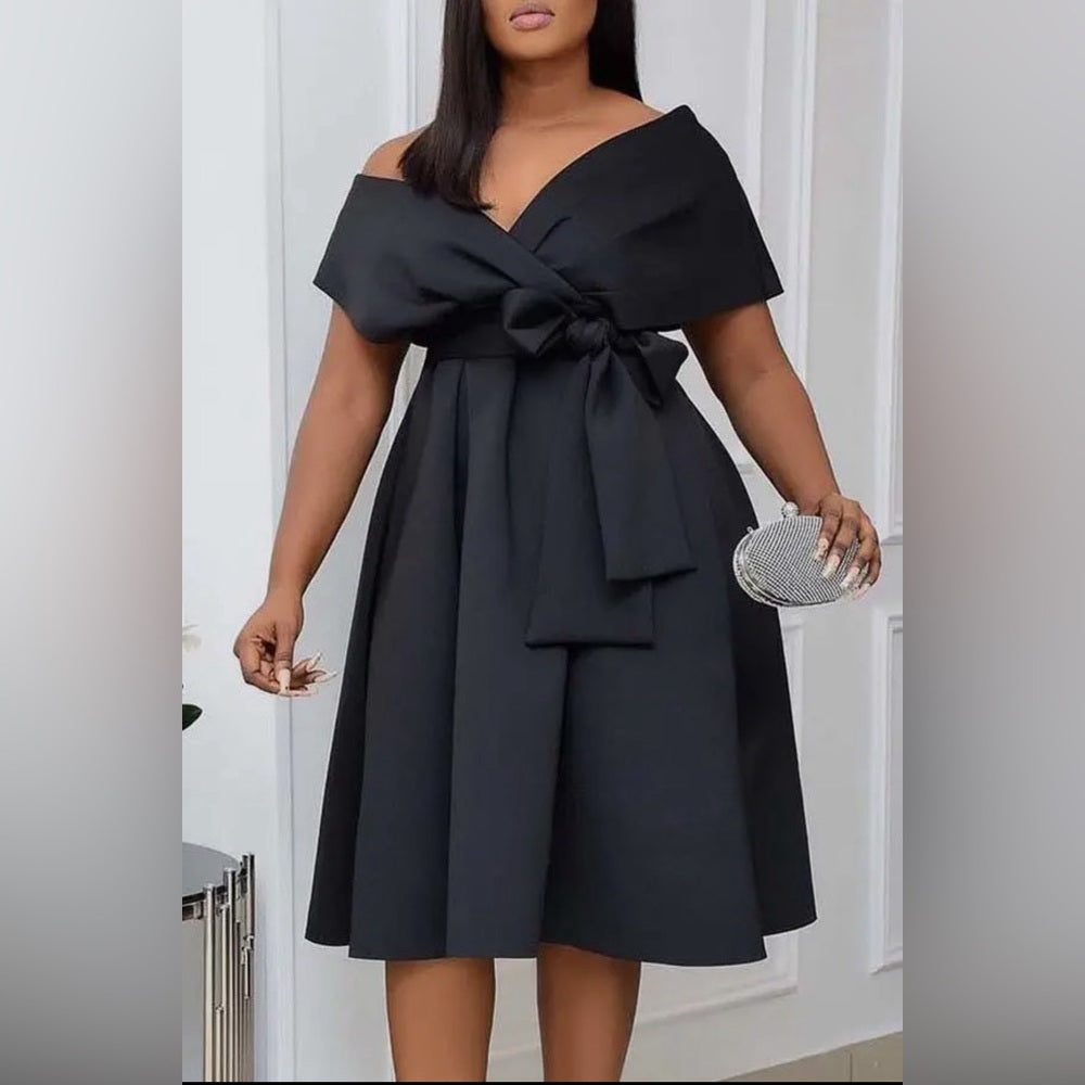 Black off-shoulder dress with a bow detail worn by a model indoors.