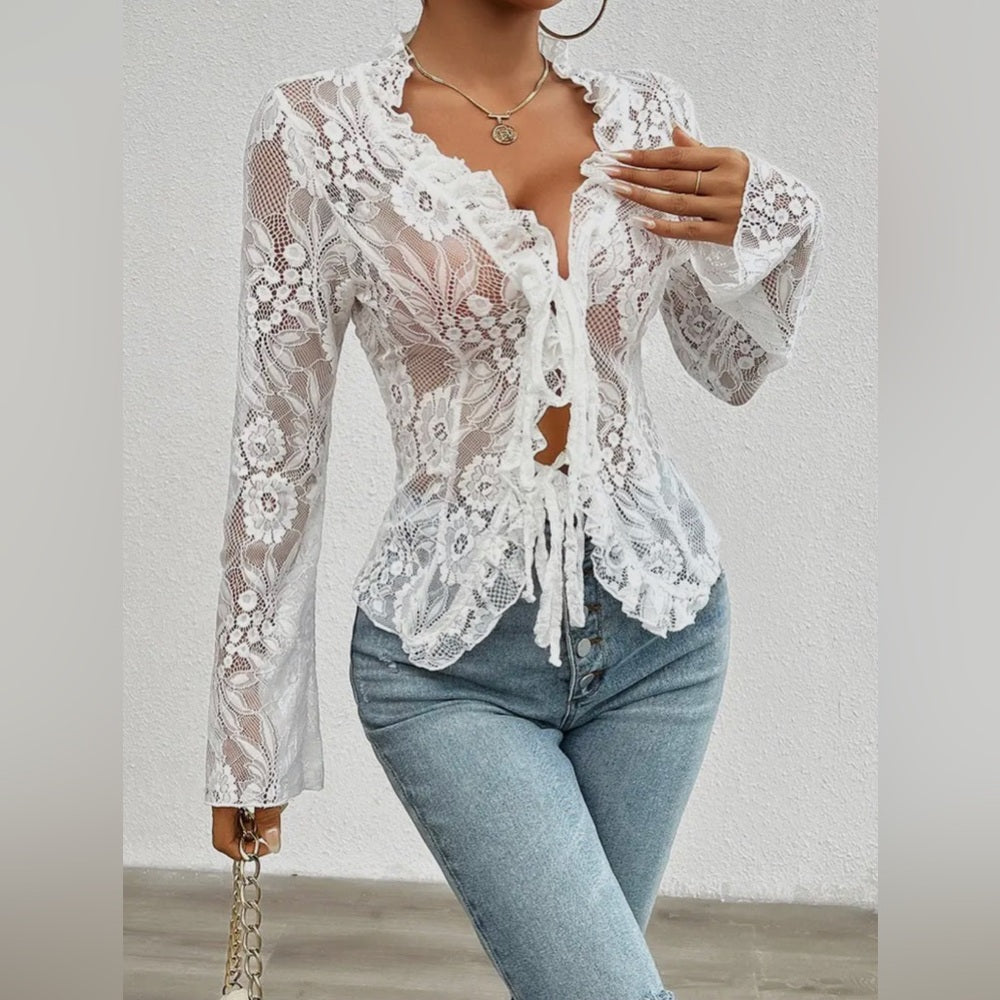 White lace top worn over a black top with blue jeans on a plain background