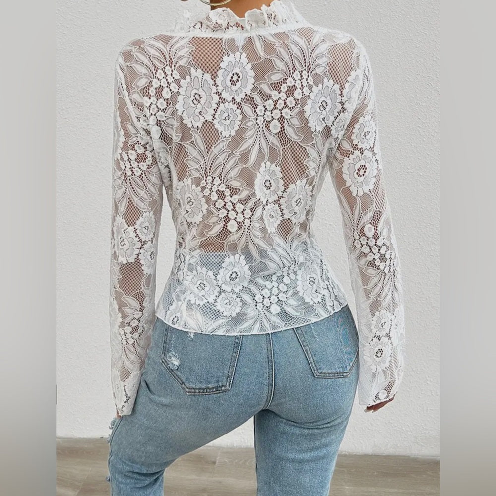 White lace top worn over a denim outfit on a plain background